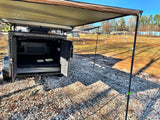 This compact RV rental features an open rear revealing a bed, with an awning extended over a gravel outdoor area.