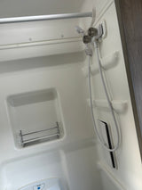 Bright, compact RV rental bathroom: white shower stall with handheld shower, toilet, and wire storage rack.