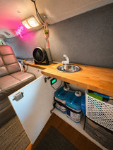 Inside this RV rental: a practical kitchen setup with a sink, hidden water tanks, a fan, & a glowing 'inspire' sign.