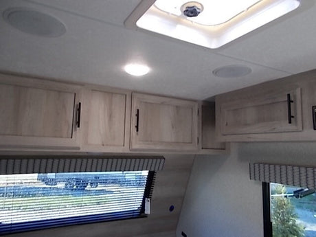 Inside your RV rental: bright, clean overhead cabinets, ceiling speakers, and a skylight creating a comfortable living space.