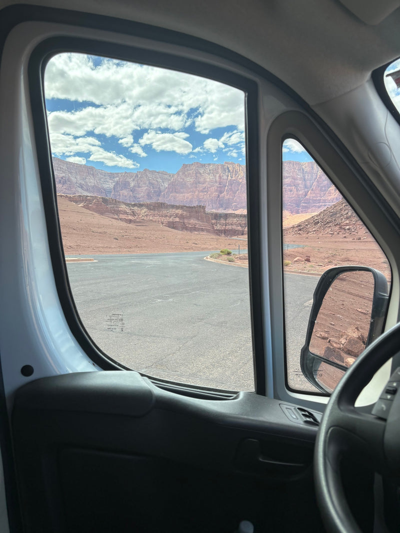 View from an RV rental's driver side window showing vast red rock canyons, a paved road, and a cloudy blue sky. — photo 20