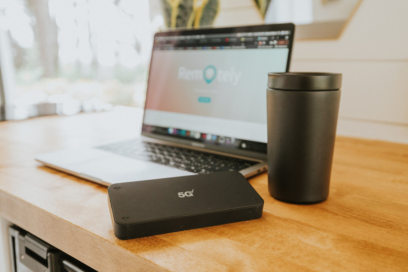 rv rental mobile office setup: A 5G device, laptop showing 'Remotely,' and mug on a wooden desk. — photo 10