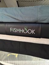RV rental interior: black upholstery with "FISHHOOK" embroidered, featuring a green line and hook. Blue blanket & window hint at outdoor travel.