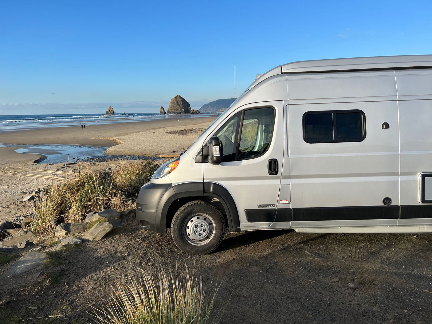 Silver RV rental parked near iconic Haystack Rock on Cannon Beach, Oregon Coast, with vast ocean views.