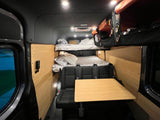 Cozy RV rental interior featuring bunk beds, a seating area with a table, and wooden paneling, ideal for travel.