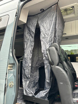RV rental interior: Gray fabric privacy enclosure, black passenger seats, and open side door visible in this camper van.