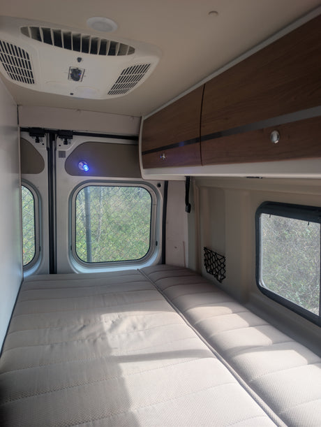 RV rental interior featuring a bed, overhead storage, AC unit, and side windows with outside views.