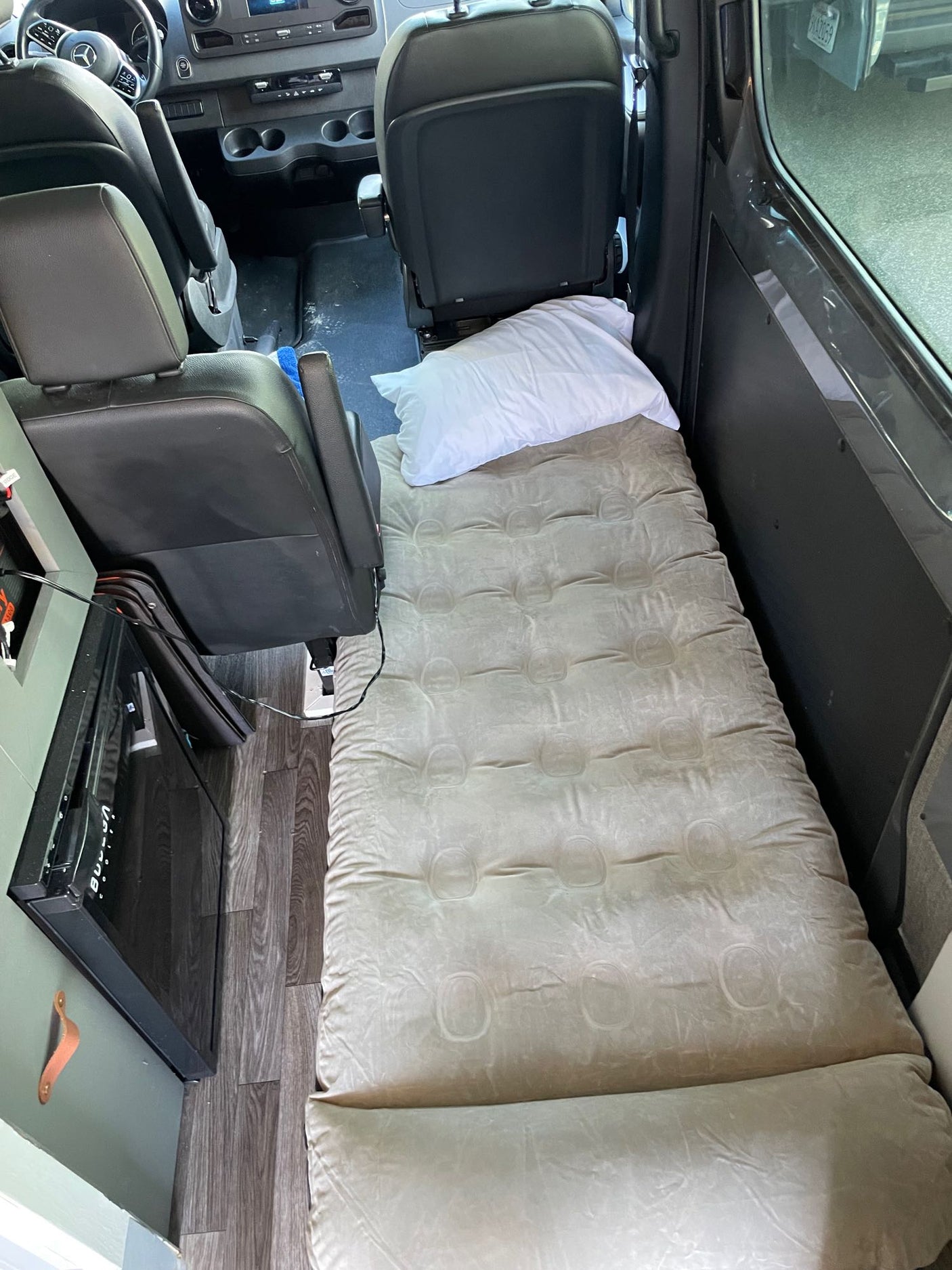 RV rental interior: Air mattress bed with pillow setup, perfect for resting during road trips. Van features seats & mini-fridge.