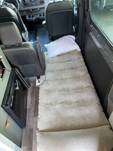 RV rental interior: Air mattress bed with pillow setup, perfect for resting during road trips. Van features seats & mini-fridge.