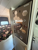 Cozy RV rental interior with a bed, custom storage, and a decorated Ever*Chill refrigerator adorned with mirrors and magnets.