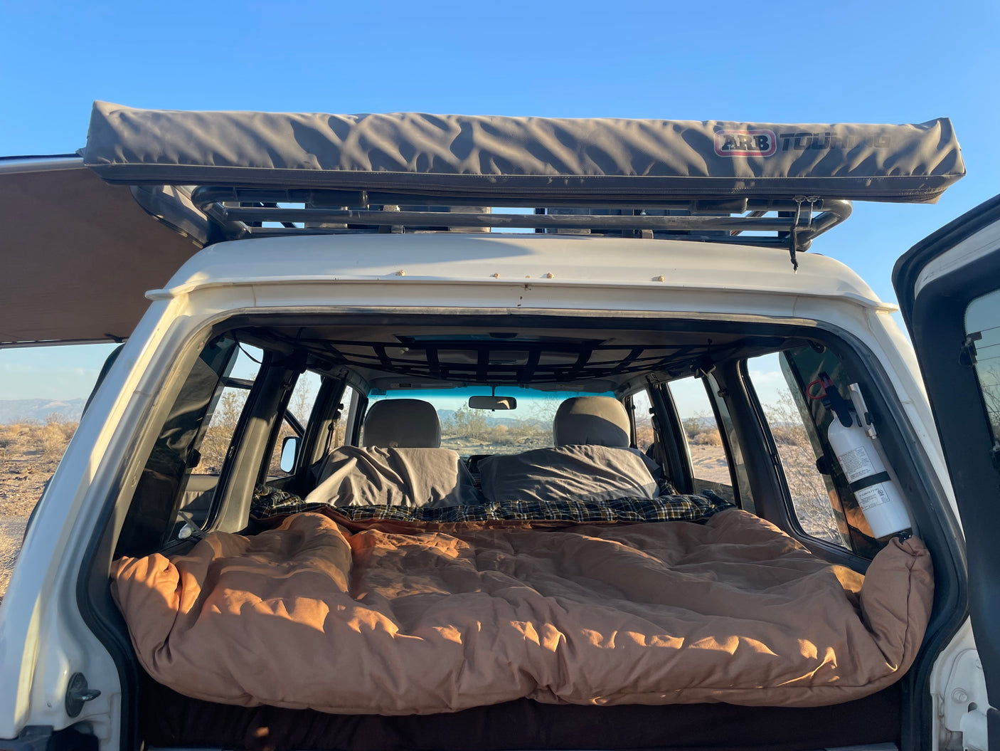 View into the rear of a white SUV with a bed setup for car camping, featuring a roof-mounted ARB awning, ideal for an rv rental trip.