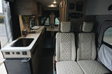 Inside a stylish RV rental, featuring a compact kitchen with cooktop, sink, fridge, and plush seating.