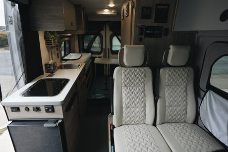 Inside a stylish RV rental, featuring a compact kitchen with cooktop, sink, fridge, and plush seating.