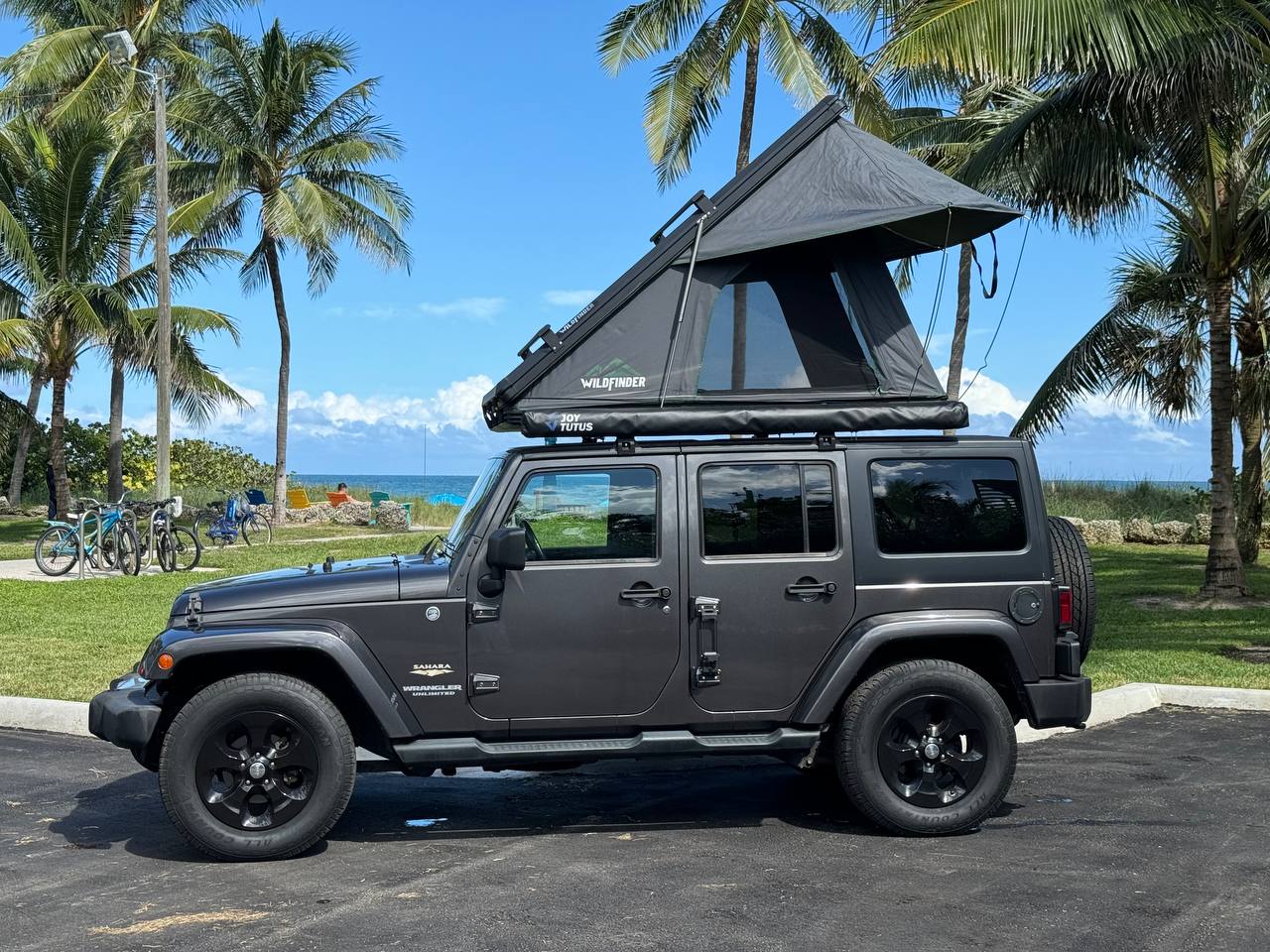 Explore the coast! This gray Jeep Wrangler with an open rooftop tent offers a unique rv rental camping experience by the beach. — photo 12