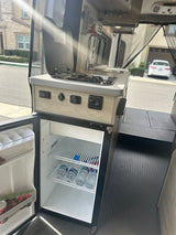 This RV rental's compact kitchen boasts a sink, stove, and a stocked fridge, ready for any adventure.