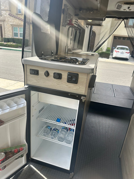 This RV rental's compact kitchen boasts a sink, stove, and a stocked fridge, ready for any adventure.