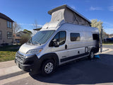 This silver pop-top camper van, branded "Pixel" and ideal for an rv rental, is parked outdoors on a sunny day.