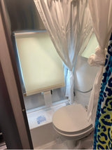 This RV rental's compact bathroom features a toilet, integrated shower, and mirror, optimized for small spaces.