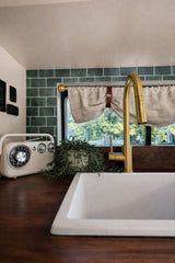 Cozy RV rental kitchen: white sink, gold faucet, wood counter, vintage radio, plant & green tiles. Perfect for travel!
