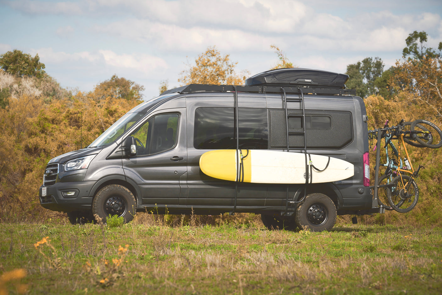 Adventure-ready grey RV rental van, fully equipped with surfboard, bikes, and a roof box for your next outdoor journey.