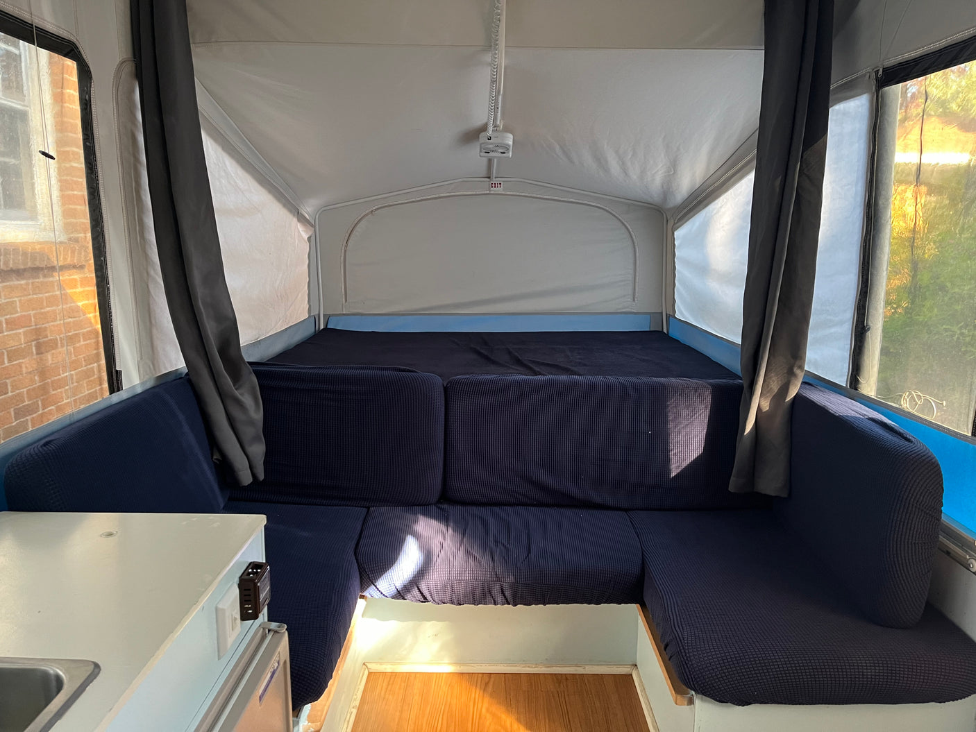 RV rental interior: blue upholstered seating, a bed, and bright windows, offering a cozy and functional space.