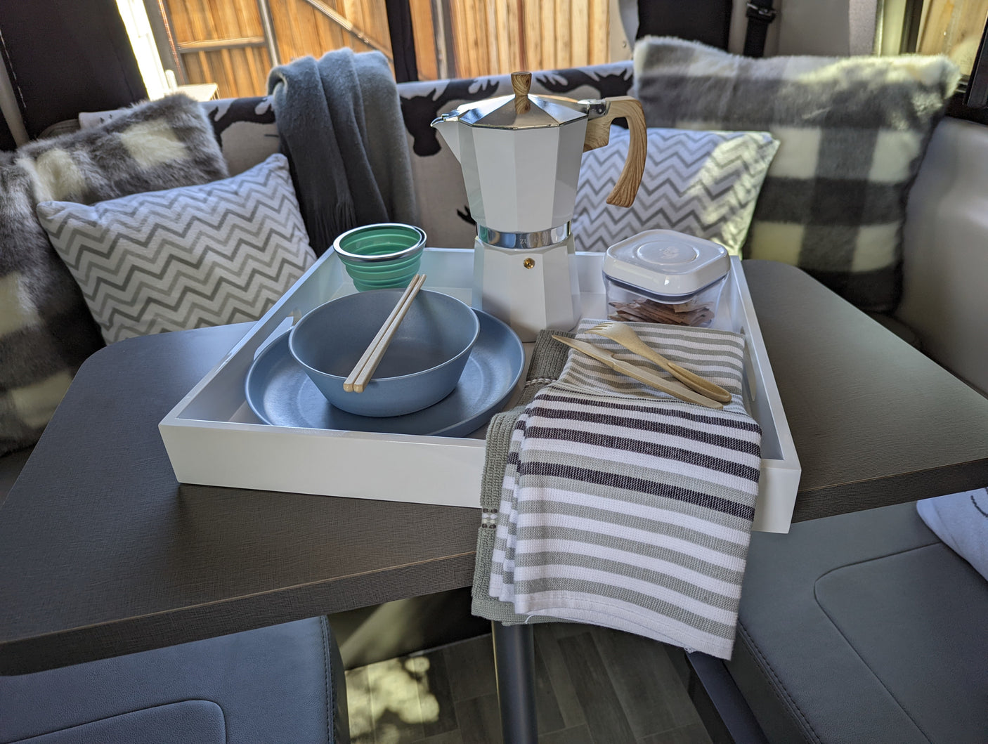 RV rental interior showing a breakfast setup on a table: a white tray with a moka pot, dishes, and sustainable utensils.