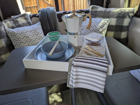 RV rental interior showing a breakfast setup on a table: a white tray with a moka pot, dishes, and sustainable utensils.