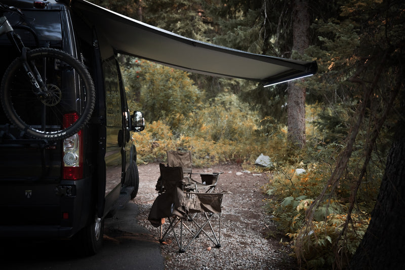 Relaxing rv rental campsite scene: dark camper van with bike, extended awning, and camp chairs among trees. — photo 5