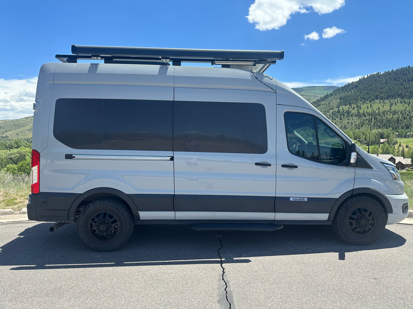 Discover nature with this custom gray Vandoit camper van, an ideal RV rental featuring rooftop gear, by mountains.