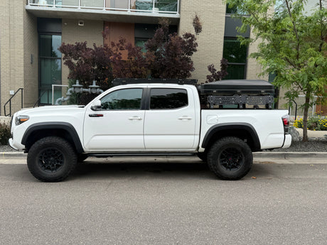 A white Toyota Tacoma TRD Pro pickup truck with a rooftop tent, an overlanding rig ready for adventure, like an RV rental.