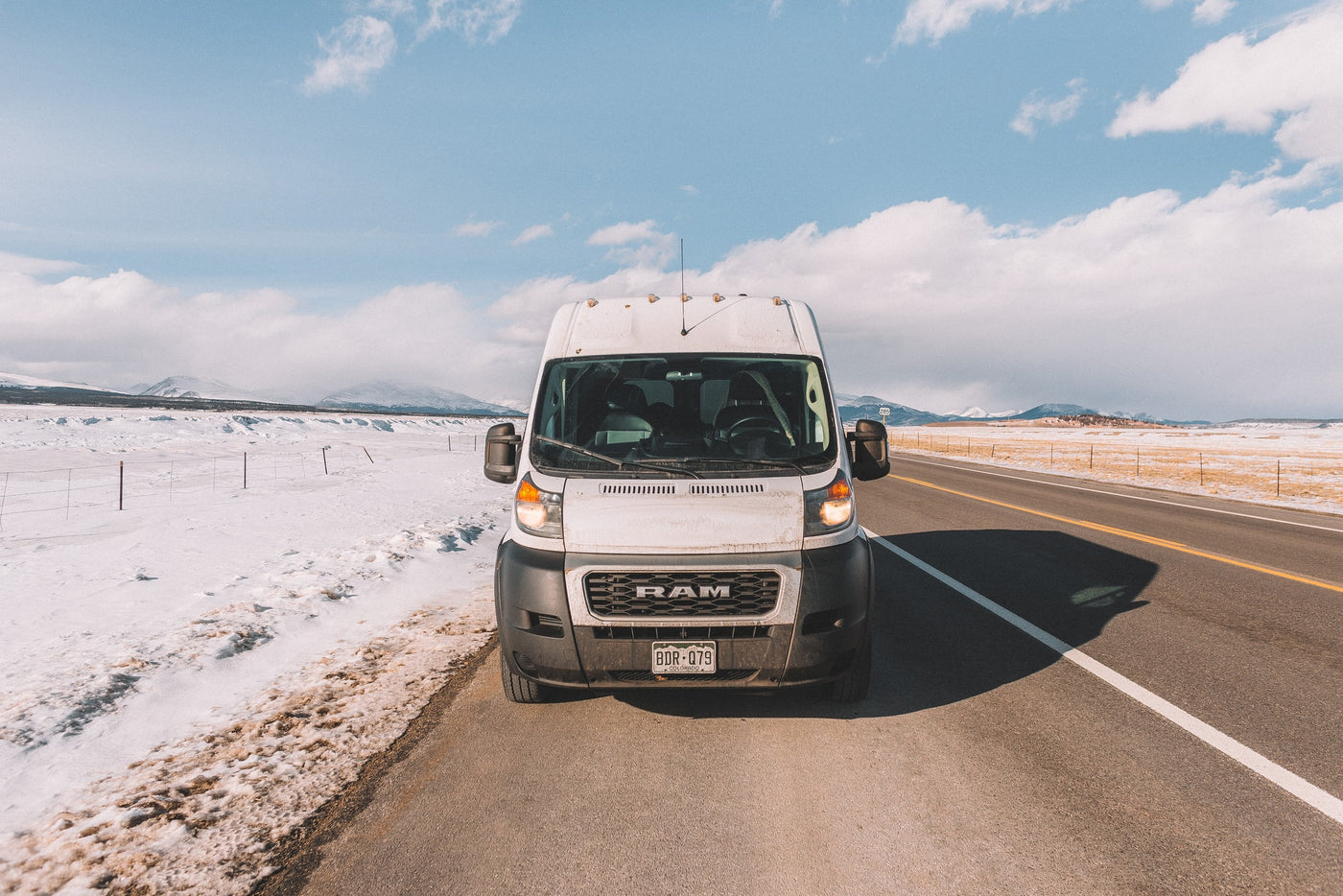 White **RV rental** van parked on snowy Colorado roadside, framed by mountains and blue sky. — photo 10