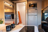 Cozy RV rental interior with kitchen (cooktop, microwave, fridge), bathroom, and a laptop workspace by the window.