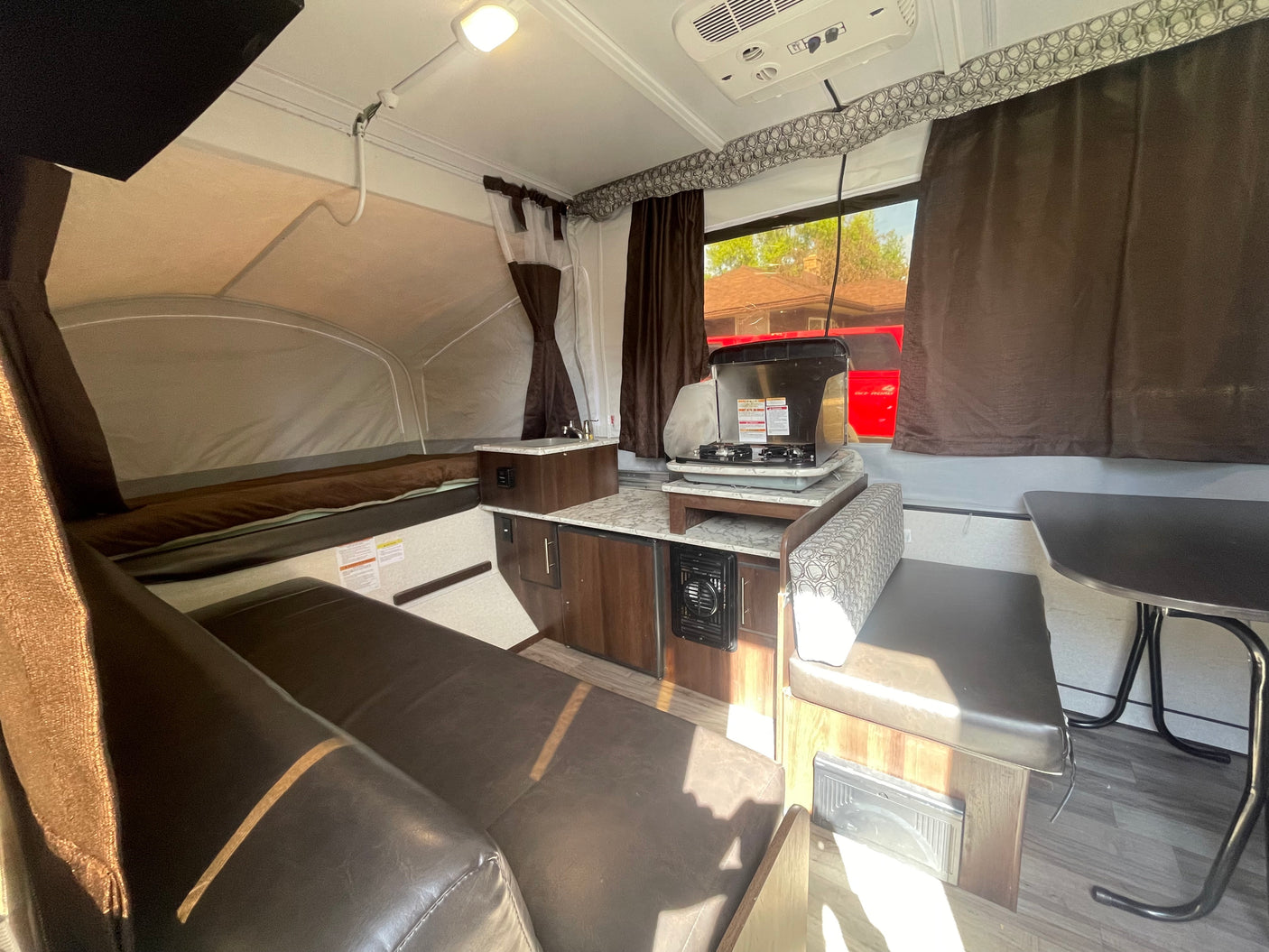 Inside this pop-up camper rv rental: a compact kitchen with stove, sink, adjacent dining area, and a comfortable bed.