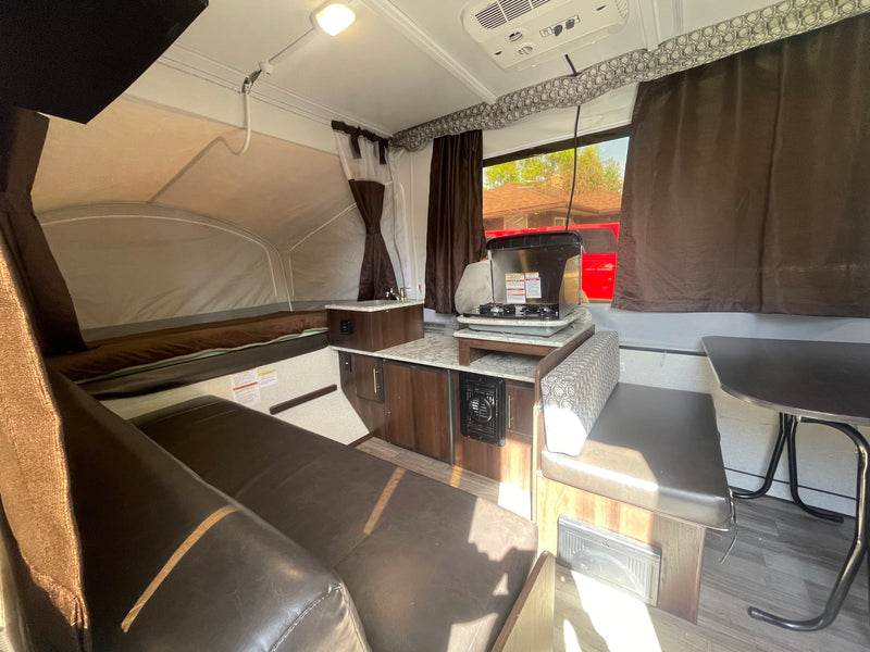 Inside this pop-up camper rv rental: a compact kitchen with stove, sink, adjacent dining area, and a comfortable bed. — photo 5