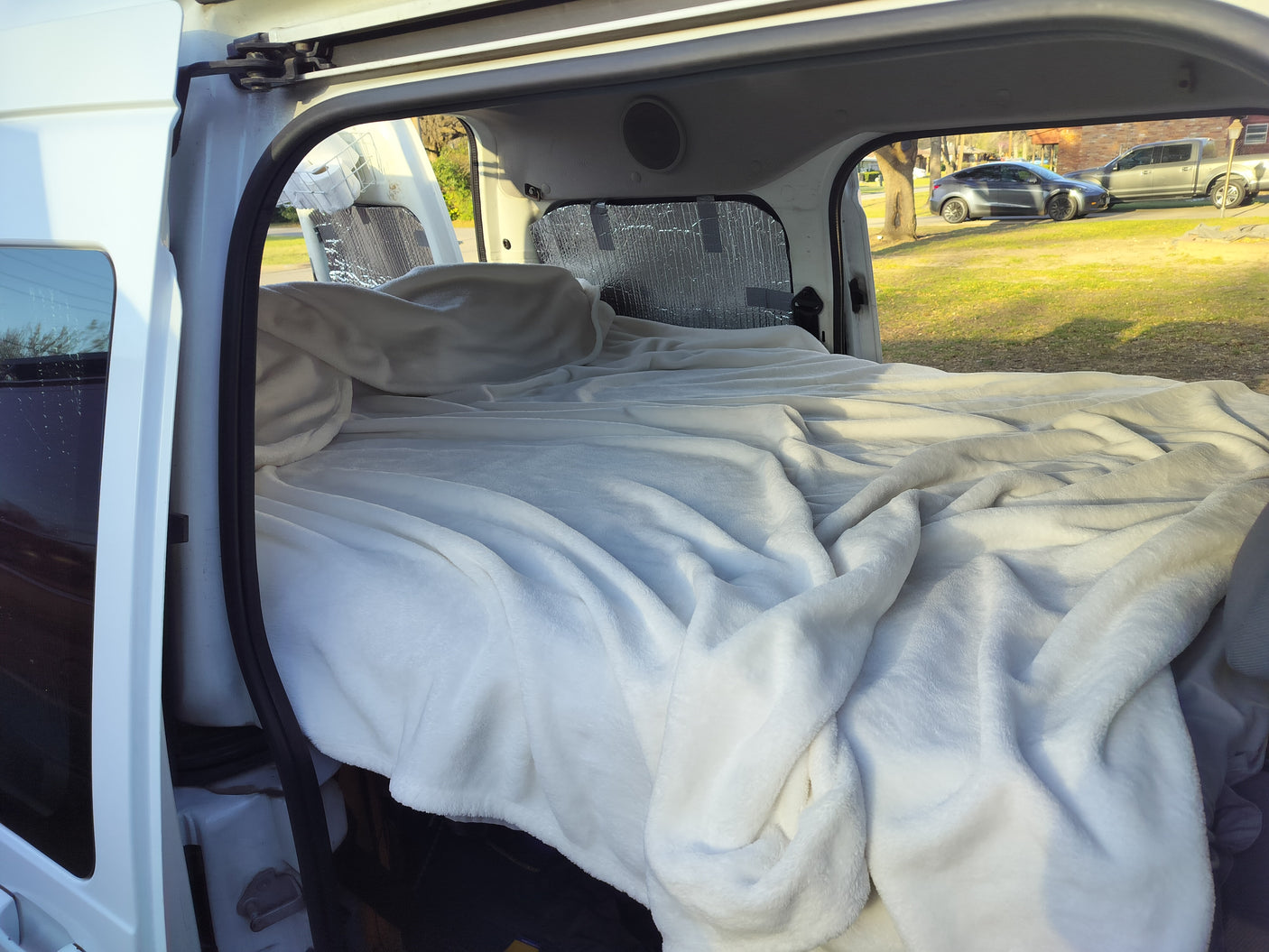 Inside an RV rental: a plush bed inside a converted van, with views of the sunny outdoors. Ready for van life!