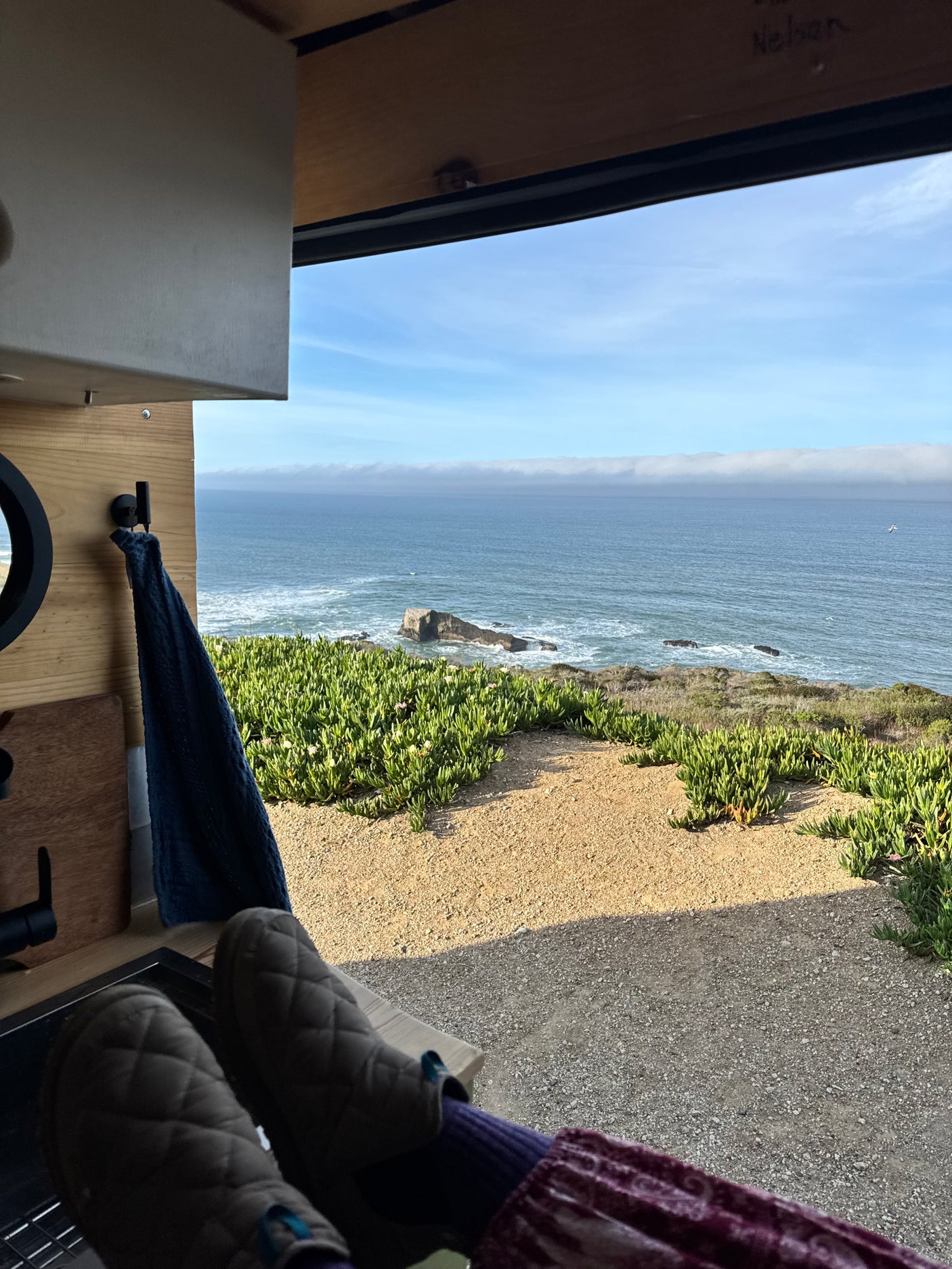 Relaxing in an RV rental, feet up, enjoying the incredible ocean view with sea stacks & lush coastal plants from inside the van.