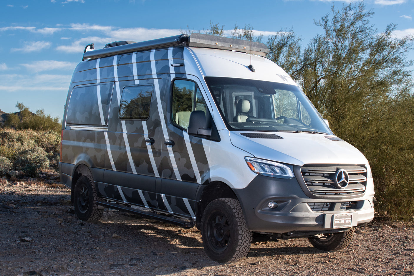 Silver Mercedes Sprinter rv rental camper van with a unique camo wrap on a desert dirt road. Adventure awaits!