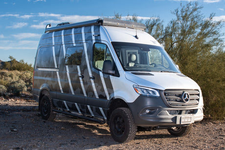 Silver Mercedes Sprinter rv rental camper van with a unique camo wrap on a desert dirt road. Adventure awaits!