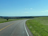 Explore vast landscapes with an RV rental. A scenic road curves past striking badlands formations under a blue sky.