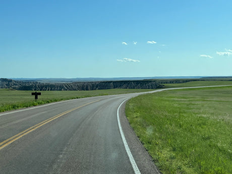 Explore vast landscapes with an RV rental. A scenic road curves past striking badlands formations under a blue sky.