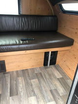 Clean rv rental interior with comfy brown seating, light wood walls, and modern wood-look floor. Remote and vents shown.