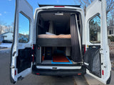 Rear view of an open white RV rental camper van, revealing a comfortable built-in bed and ample interior storage for adventures.