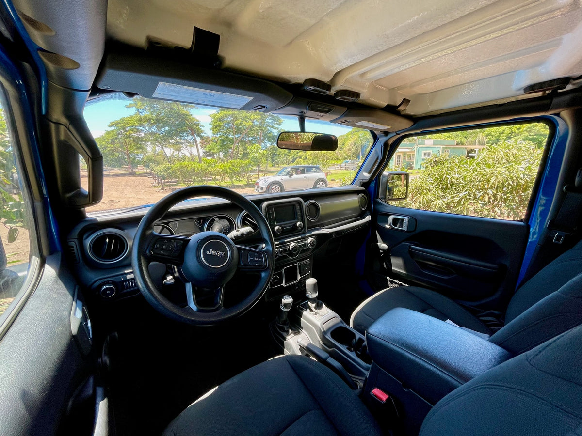 The spacious interior of a blue Jeep, showing the steering wheel and dashboard. A view outside reveals trees and a building, ready for any RV rental adventure. — photo 11