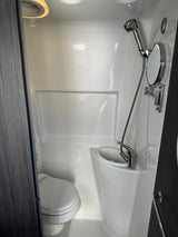 Compact RV rental wet bath with toilet, sink, shower, and adjustable mirror. Ideal for road trip convenience.