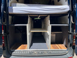 Rear view of an RV rental camper van showing an organized interior with an elevated bed, ample storage bays, and a central aisle.