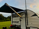 RV rental: Catalina travel trailer with illuminated awning, grill, and chair at a grassy campsite.