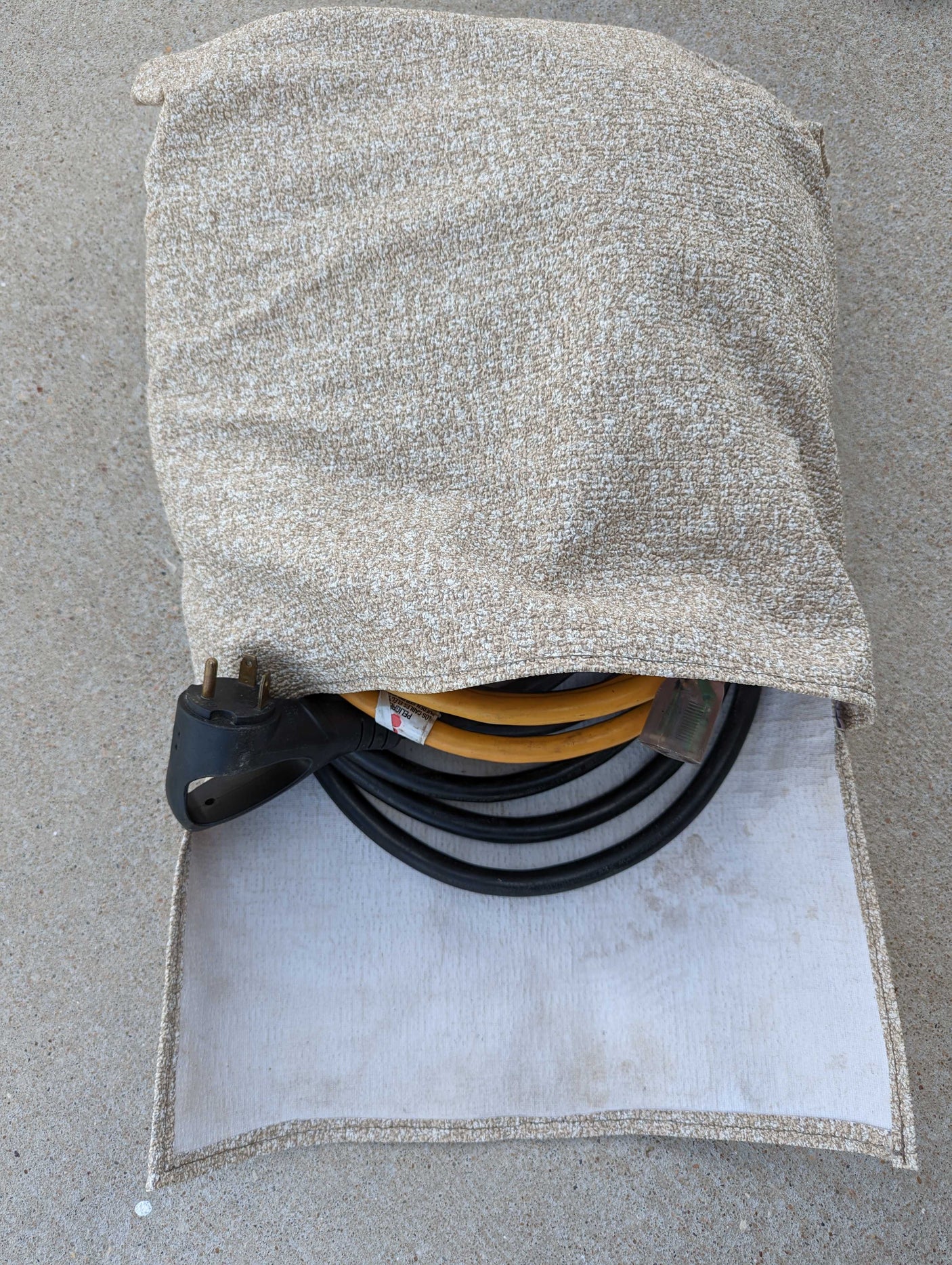 Beige fabric bag holding an RV rental power adapter & electrical cables on concrete, essential for your trip.