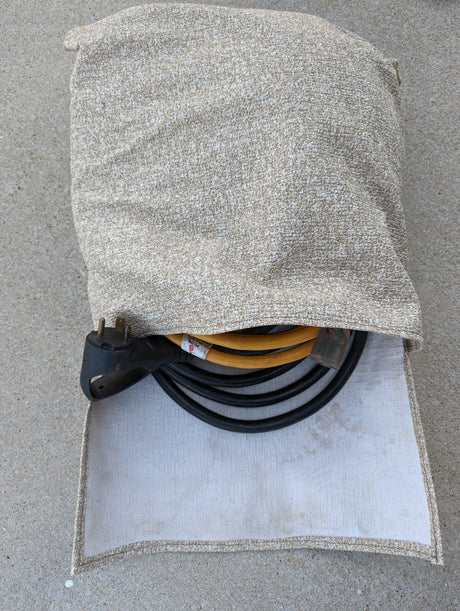 Beige fabric bag holding an RV rental power adapter & electrical cables on concrete, essential for your trip.