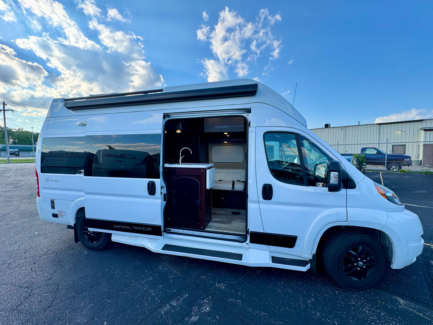 White "National Traveler" RV rental with side door open, revealing a compact interior kitchen, sink, and seating area.