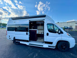 White "National Traveler" RV rental with side door open, revealing a compact interior kitchen, sink, and seating area.